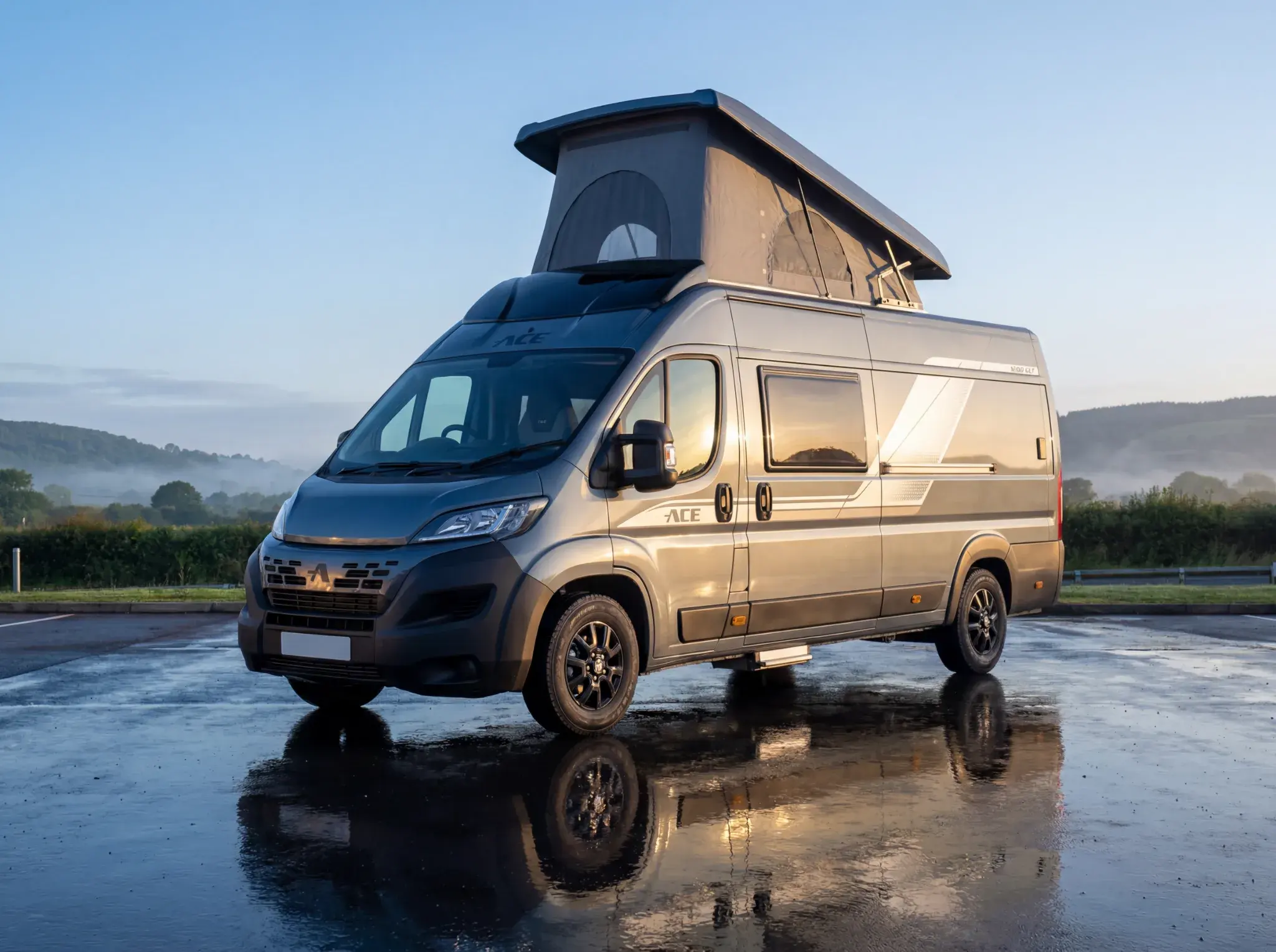 Ace motorhome with pop-up roof parked on wet ground, mountainous landscape in background.