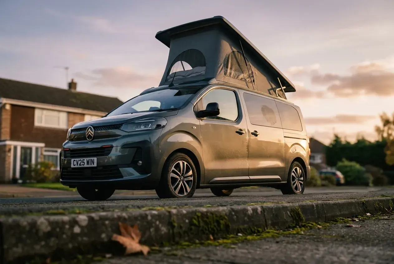 A compact Citroen Holidays pop-top campervan with its roof raised, parked on a UK driveway in warm evening light.