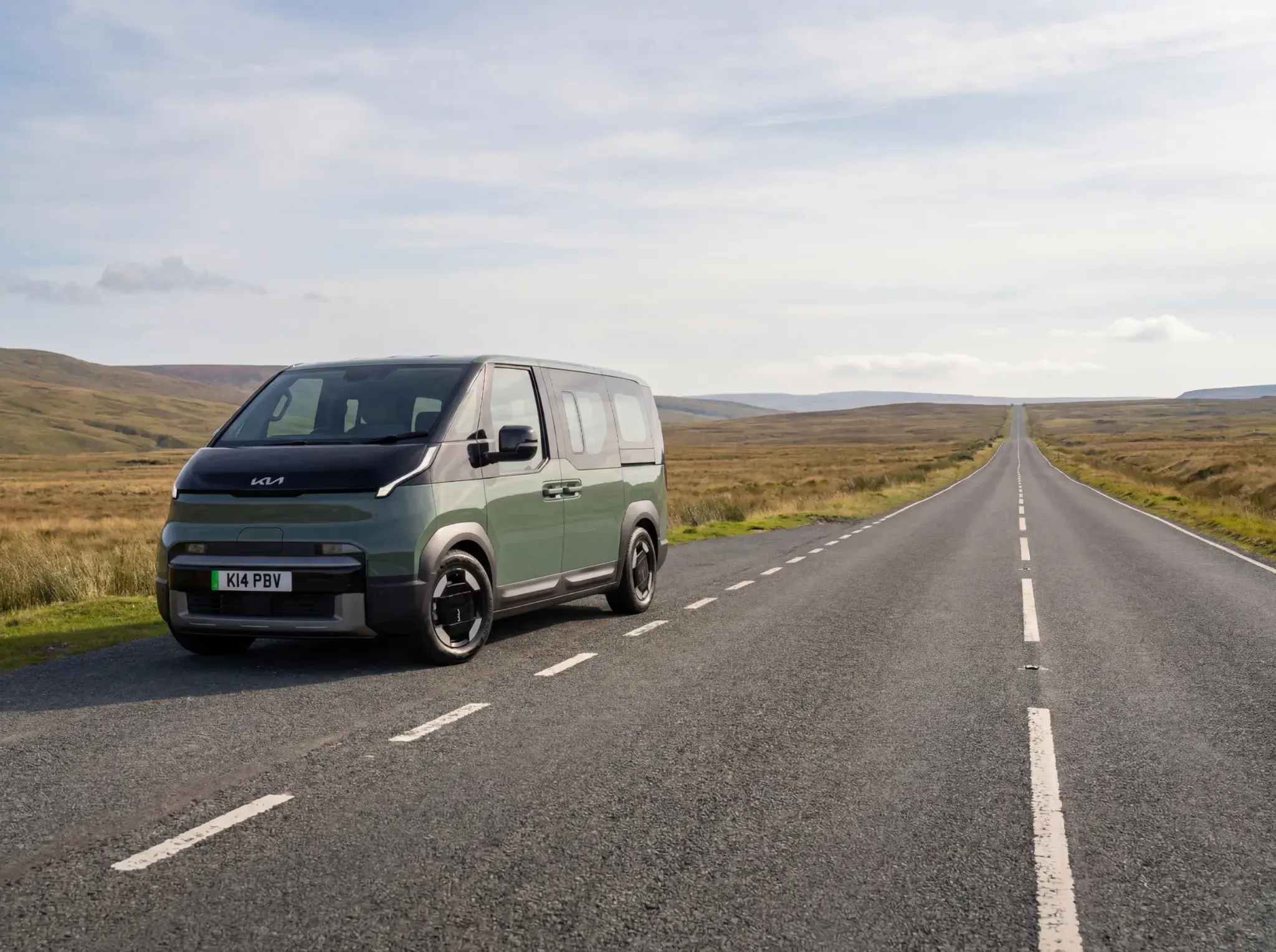 Kia EV9 electric campervan in sage green and white parked on straight rural road with moorland hills in background.