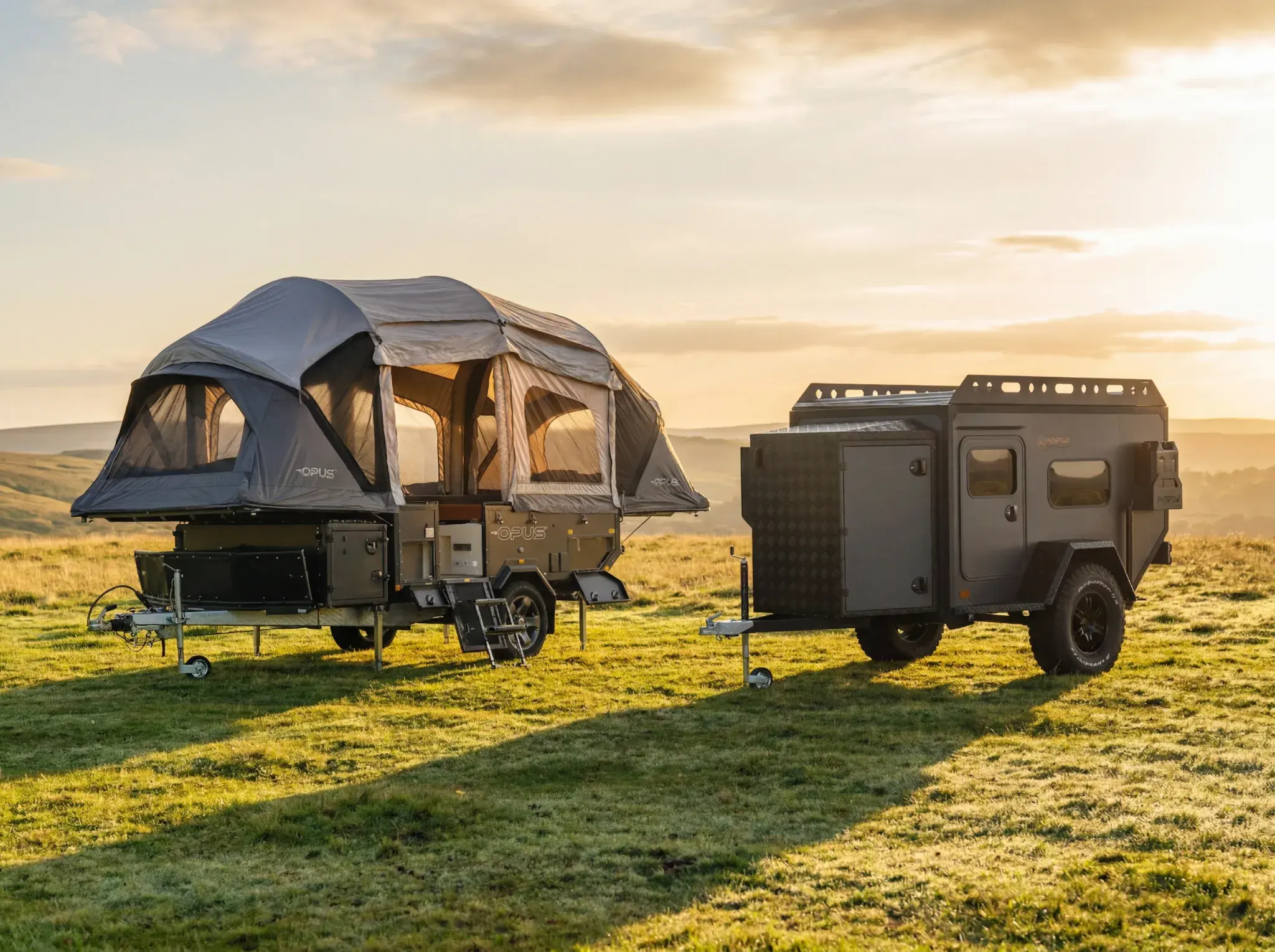 Two black compact camping trailers parked on grass with deployed tent awnings under sunset sky.