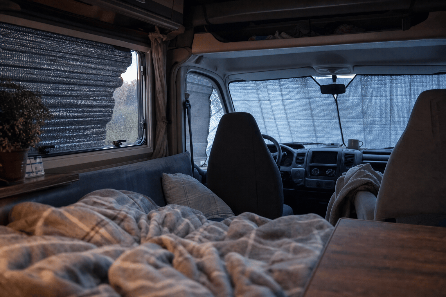 Inside a campervan at dawn with thermal blinds fitted over the cab windscreen and side windows on a frosty morning.