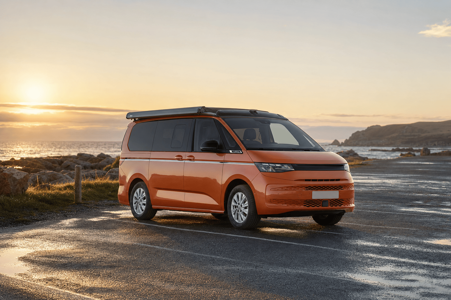 A modern VW California camper van parked alone in a coastal car park during golden-hour evening light, with the sea and a headland behind.