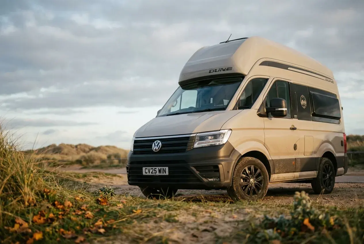 A sand-coloured VW Grand California Dune campervan with black alloy wheels parked on open ground.