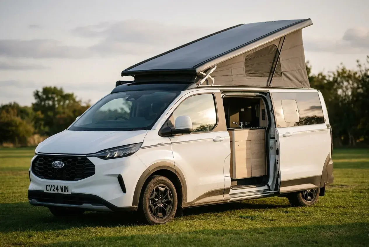 A modern Ford Transit Nugget pop-top campervan with its roof raised and side door open, parked on a grassy UK campsite at golden hour.
