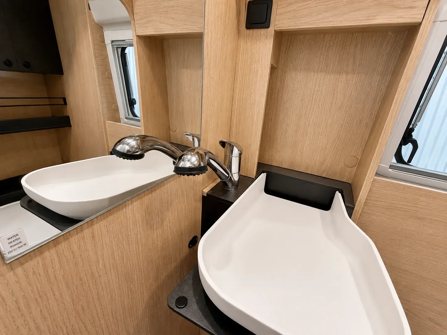 Campervan bathroom interior with two white ceramic sinks, chrome fixtures, and natural wood cabinetry.