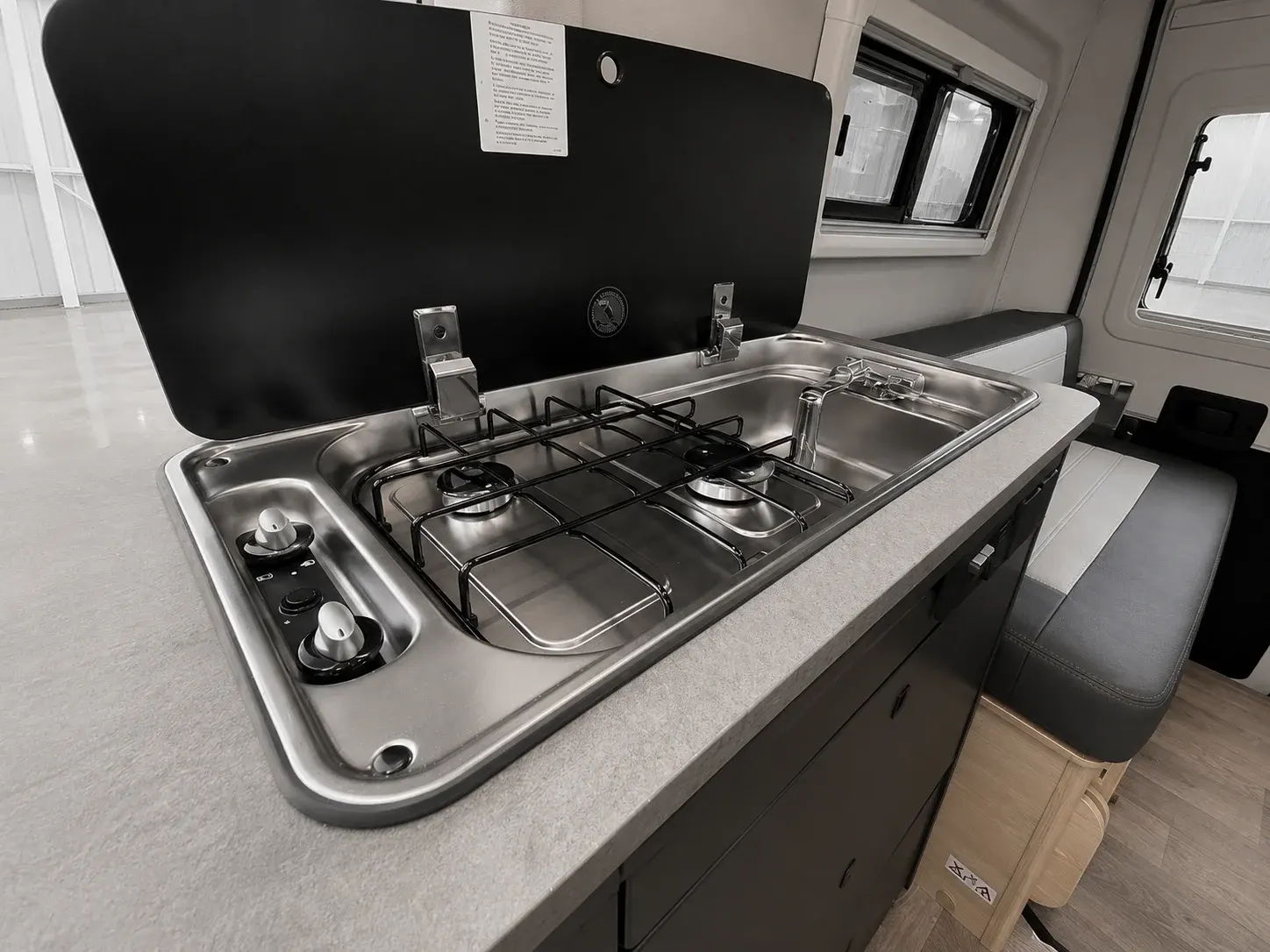 Campervan kitchen interior with two-burner gas hob, sink, and black splashback panel.