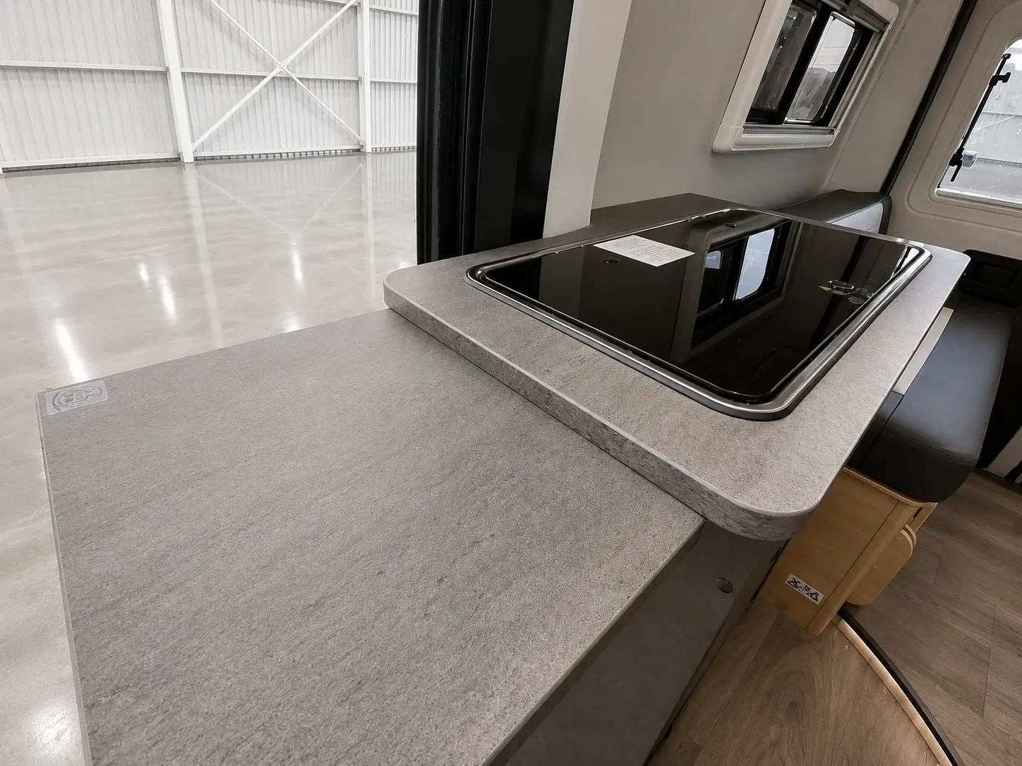 Campervan kitchen interior with grey worktops, black hob, and window overlooking white garage.