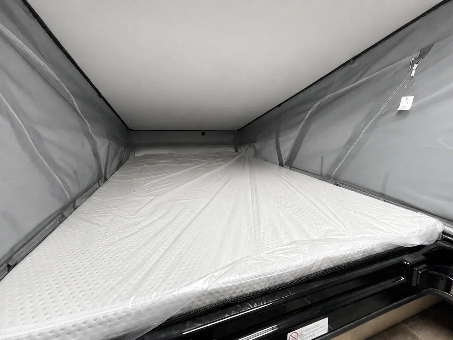 Pop-up roof tent interior with white mattress and grey fabric walls extended.