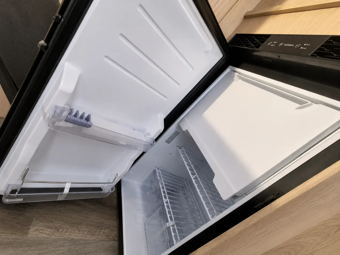 Open portable refrigerator with white interior and empty shelves on wooden floor.