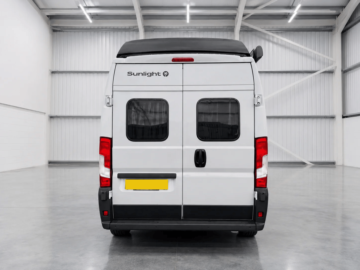 White Sunlight campervan rear view in bright garage with black roof and red tail lights.