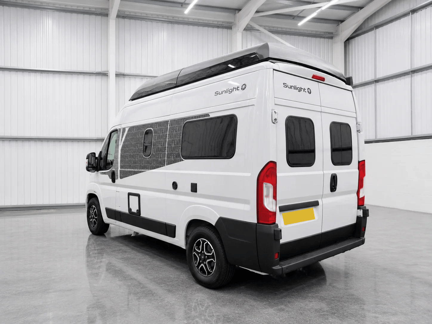 White Sunlight campervan with black roof spoiler, red tail lights, and tinted windows in warehouse setting.