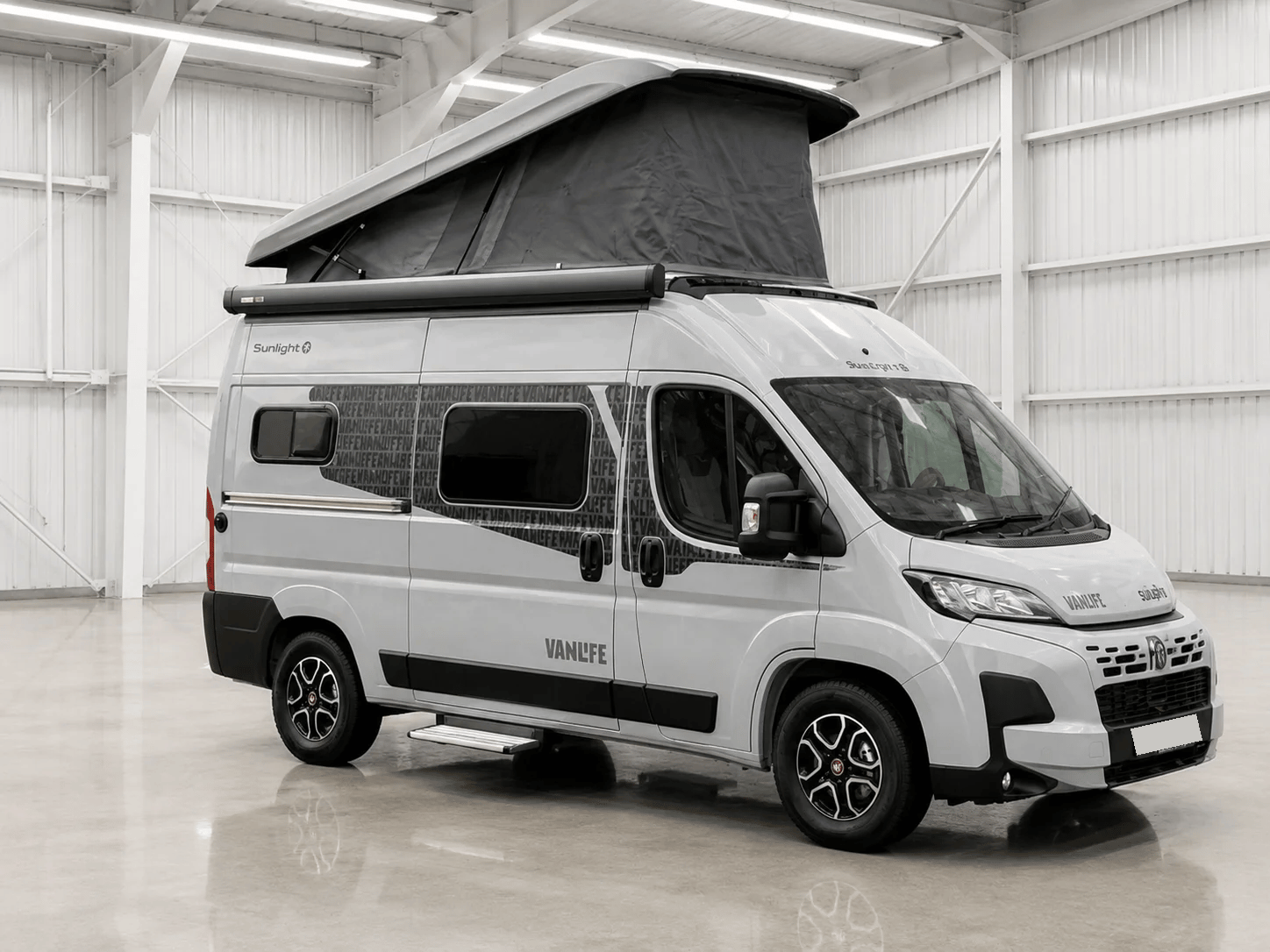 White Sunlight campervan with roof tent extended, parked in industrial warehouse with fluorescent lighting.