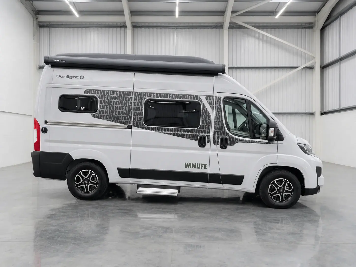 White Sunlight campervan with Thule roof rack parked in warehouse, side profile view.