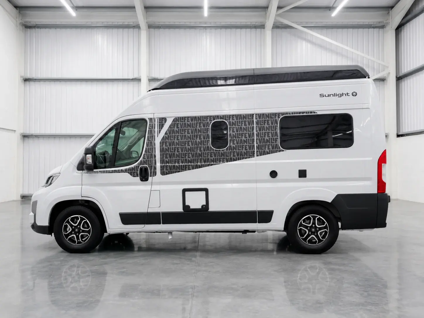 White Sunlight campervan with black roof bar and red rear lights, side profile in warehouse.