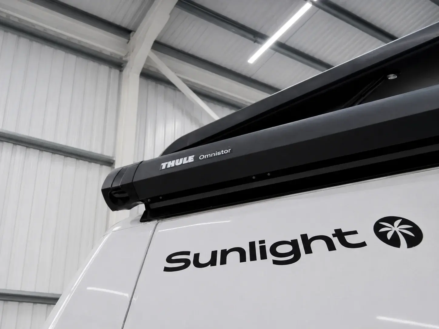 White Sunlight campervan with black Thule Omnistor roof rack in warehouse setting.