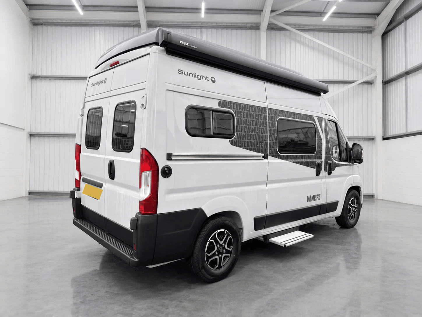 White Sunlight Vanlife campervan with roof rack, side windows, and red tail lights in showroom.