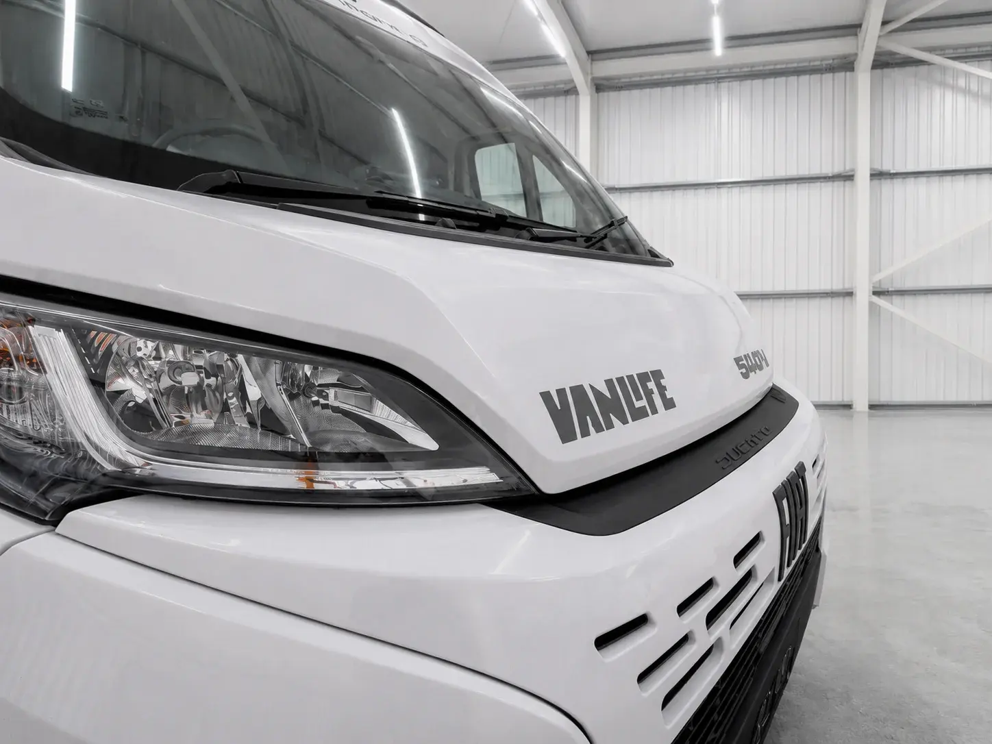 White Vanlife campervan front end with headlights and grille in warehouse setting.
